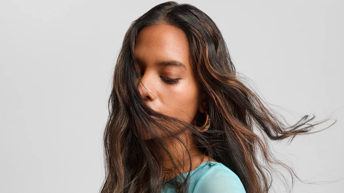 Vrouw met lang donkerbruin haar, subtiele karamel highlights en natuurlijke beweging